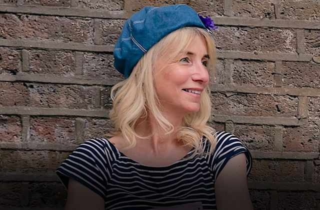 Freelance instructional designer stands in front of brick wall in beret, smiling to her left