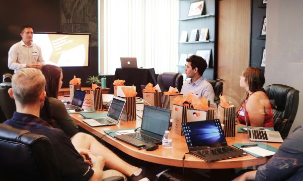 A team of people sit around a table in a meeting room watching someone present a well designed training course