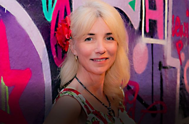 Blond instructional designer stands in front of grafitti wall wearing a rose in her hair